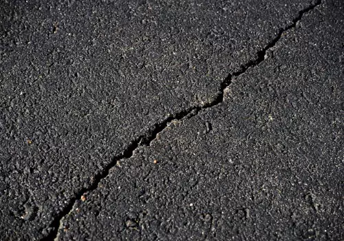 A fault is seen in an asphalt surface, ready for repair. BearCat makes and sells Crack Sealers in Kansas.